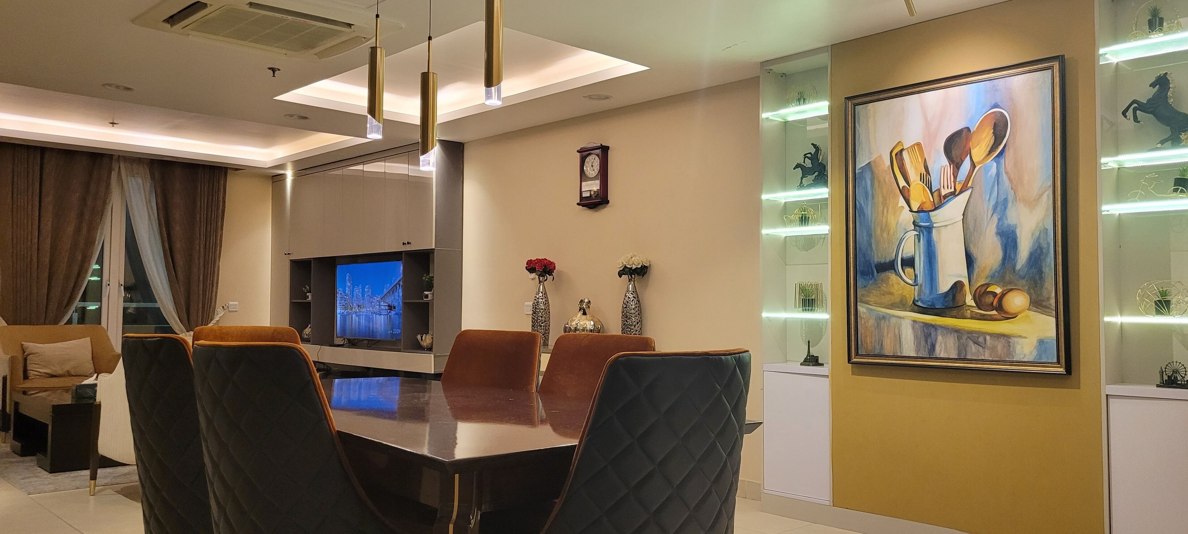 A modern dining area with a large table, comfortable chairs, a flat-screen TV, decorative items, and a painting on the wall.