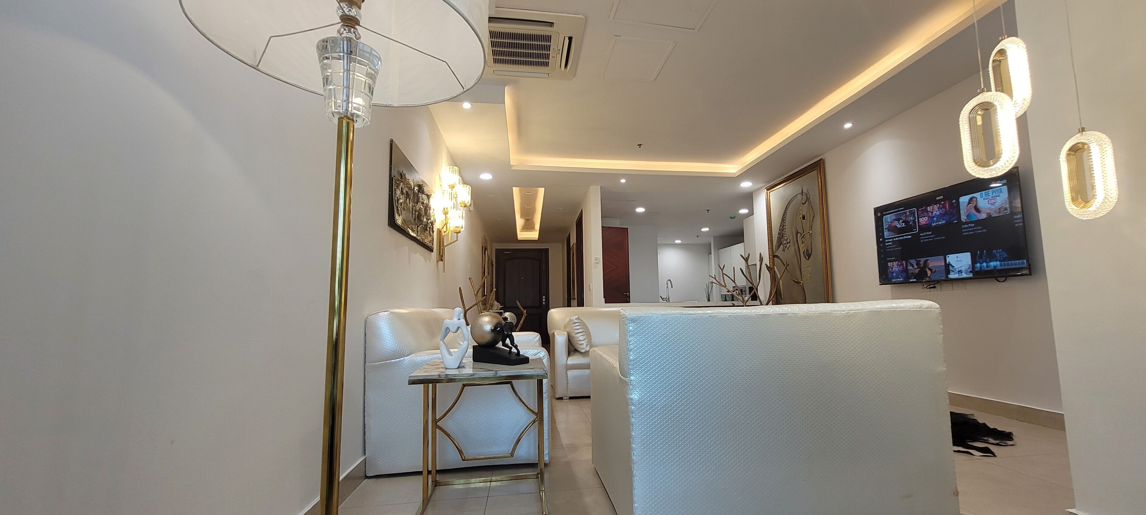 Una sala de estar moderna con un sofá blanco, una mesa de centro de vidrio y un televisor montado en la pared.