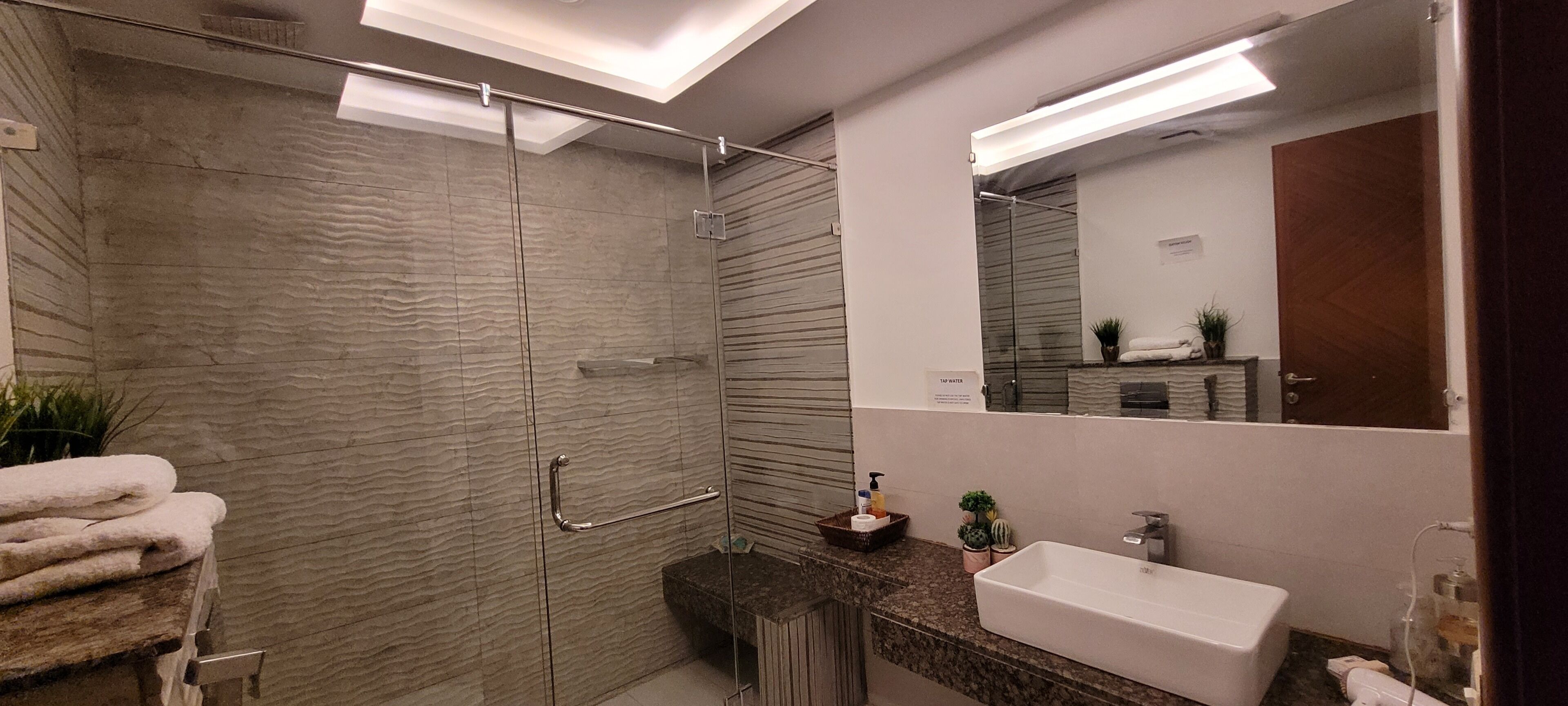 Un baño moderno con ducha envuelta en vidrio, tocador con lavabo y un espejo grande.