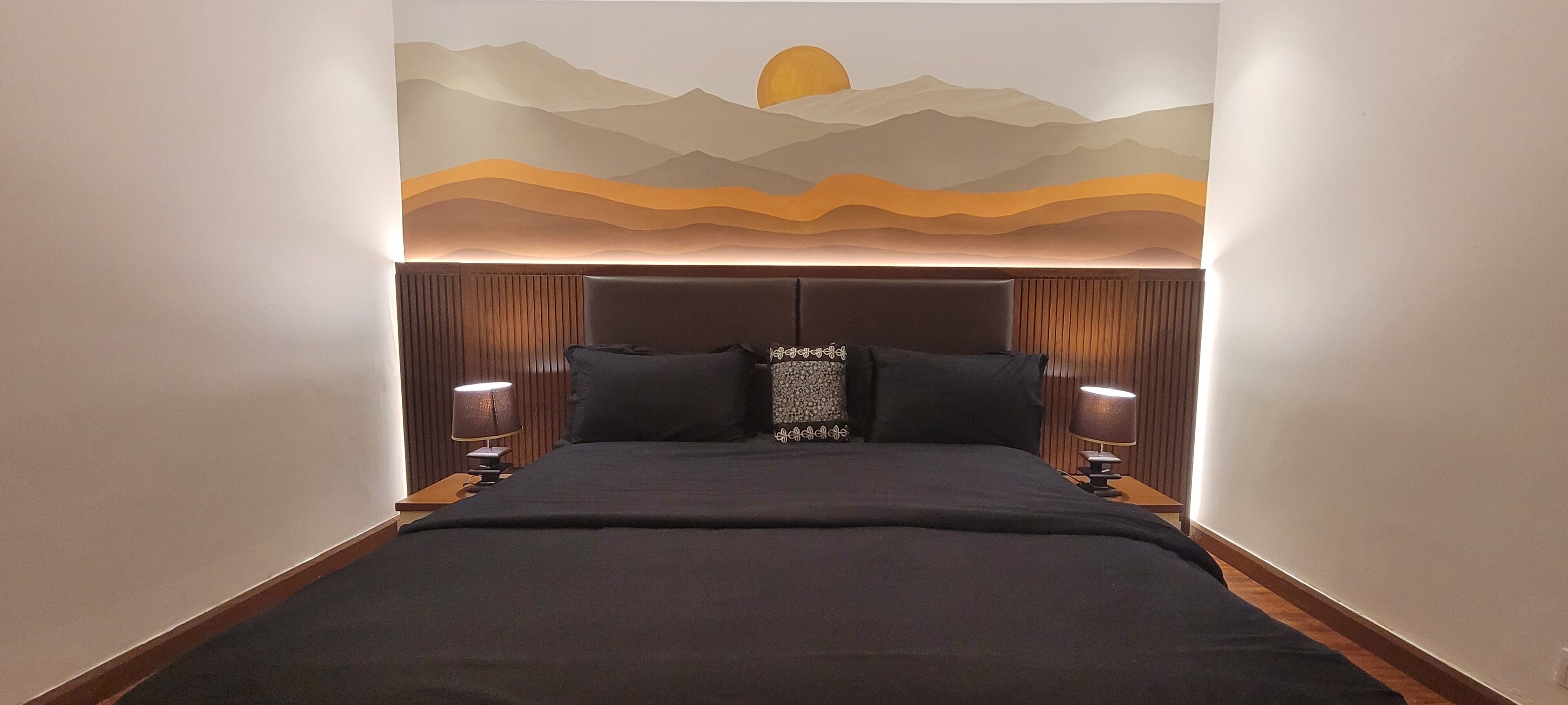 A hotel room with a bed, two bedside lamps, a wall mural, and a headboard.