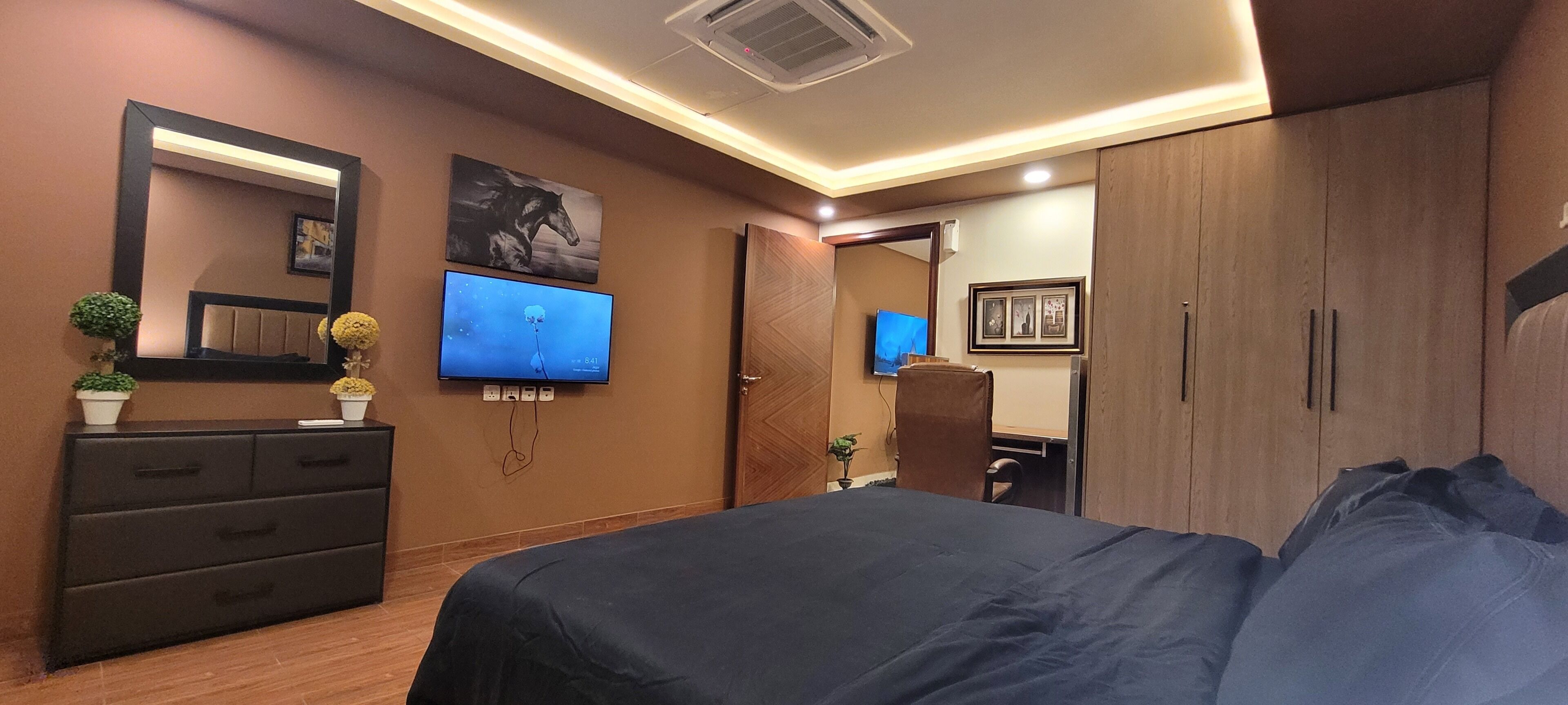A bedroom with a large bed, a dresser, a TV, and a wardrobe.