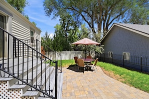 A patio with a table and chairs, a red umbrella, and a white fence. - Charming Historic Cottage • Cozy Family Getaway! (Greeley)