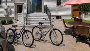A patio with a covered grill, a bicycle, a table with chairs, and a house with steps leading to the door. - Charming Historic Cottage • Cozy Family Getaway! (Greeley)