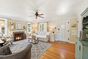 A living room with a fireplace, a ceiling fan, a sofa, a coffee table, and a patterned rug.