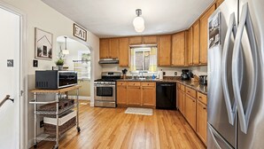 A kitchen with wooden cabinets, stainless steel appliances, and a cart with baskets. - Charming Historic Cottage • Cozy Family Getaway! (Greeley)