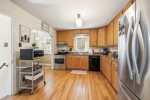 A kitchen with wooden cabinets, stainless steel appliances, and a cart with baskets.