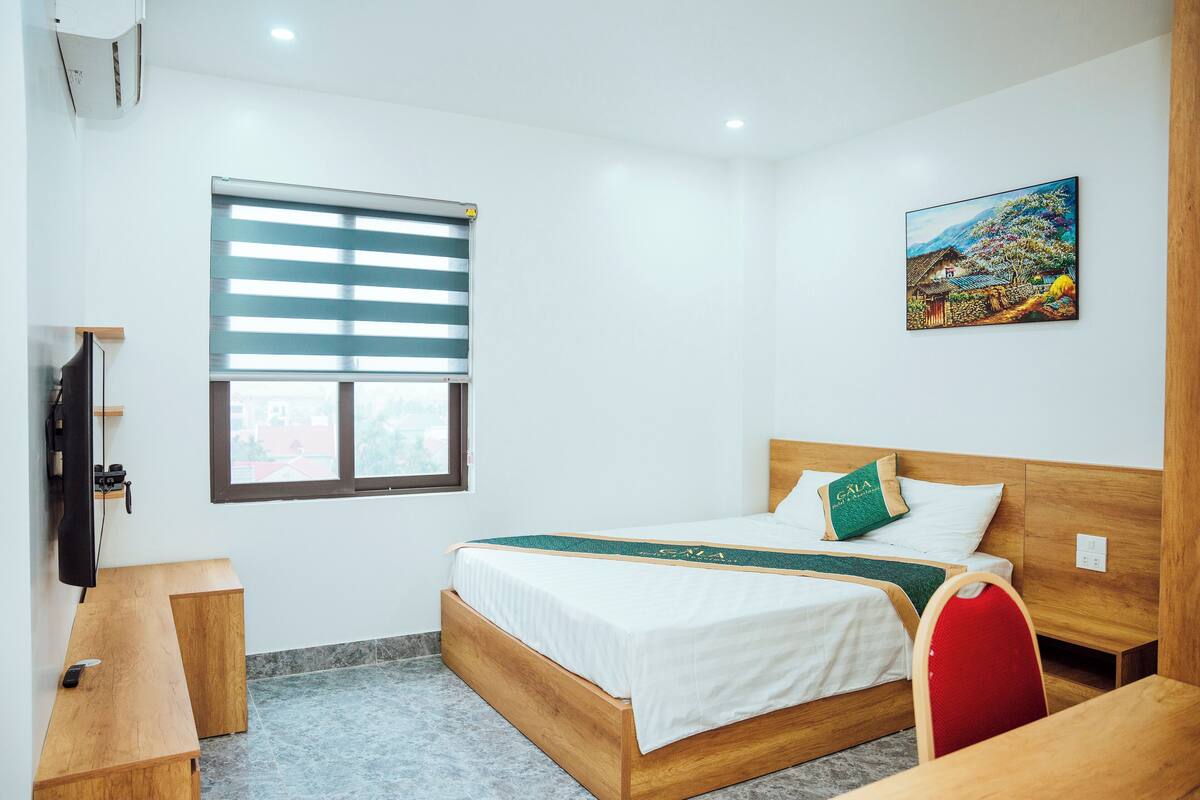 Ein Hotelzimmer mit einem Holzbett, einem Schreibtisch, einem Stuhl, einem Fernseher und einem Fenster mit Jalousien.