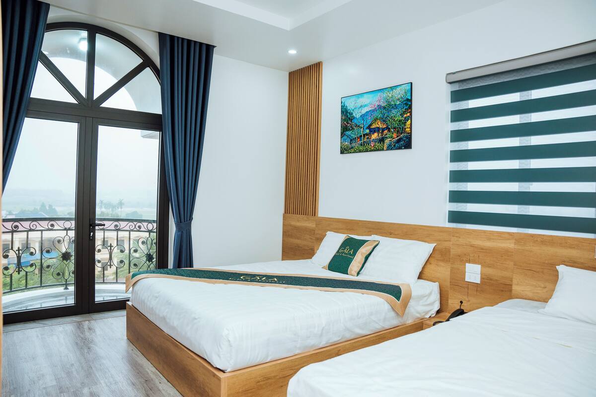 Ein Hotelzimmer mit großem Fenster, Holz-Kopfteil, einem Gemälde und Blick auf die Stadt.