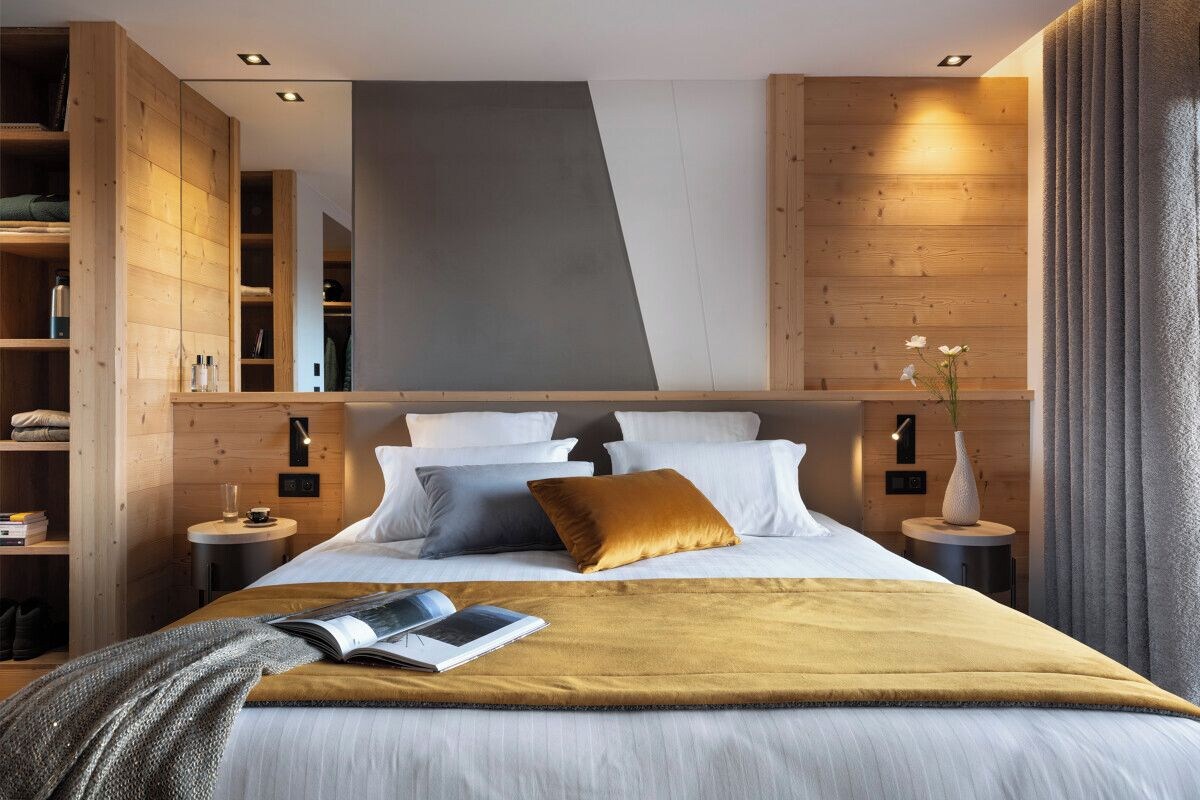 A modern bedroom with a large bed, wooden headboard, bedside tables, and a built-in wardrobe.