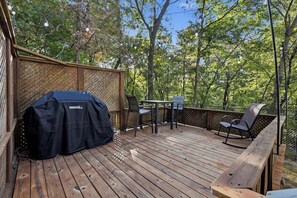 A wooden deck with a grill, chairs, and a table.