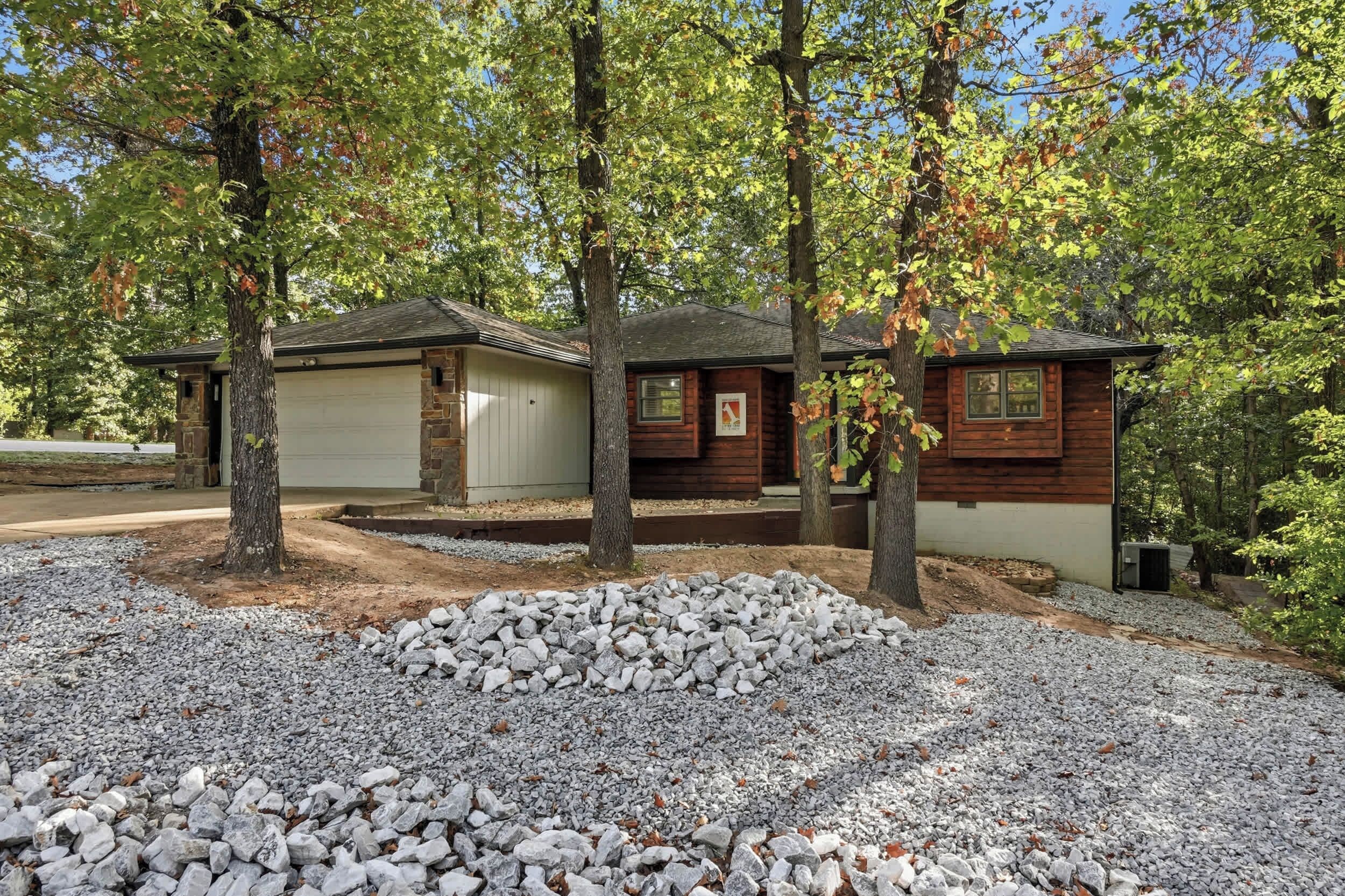 Una baita con un garage, immersa tra gli alberi e un vialetto sterrato.