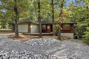 A cabin with a garage, surrounded by trees and a gravel driveway. - Bike In/Bike Out Home in Bella Vista (Bella Vista)