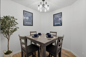 A dining area with a table set for four, two framed maps on the wall, and a potted plant.