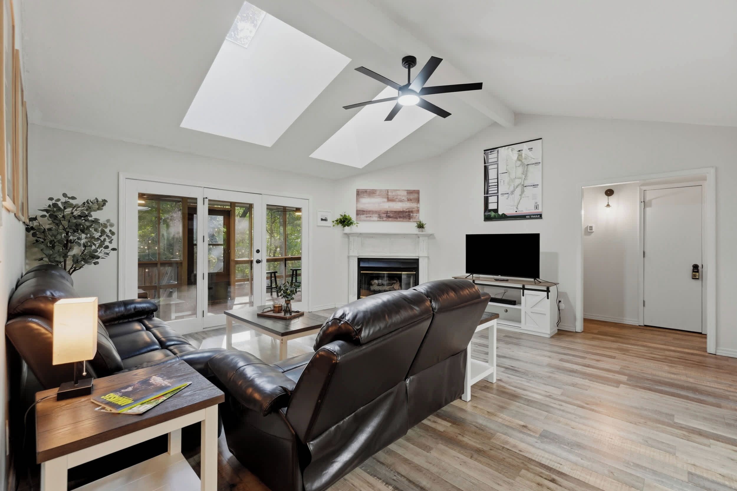 A modern living room with a leather sofa, a flat-screen TV, a fireplace, and a skylight.