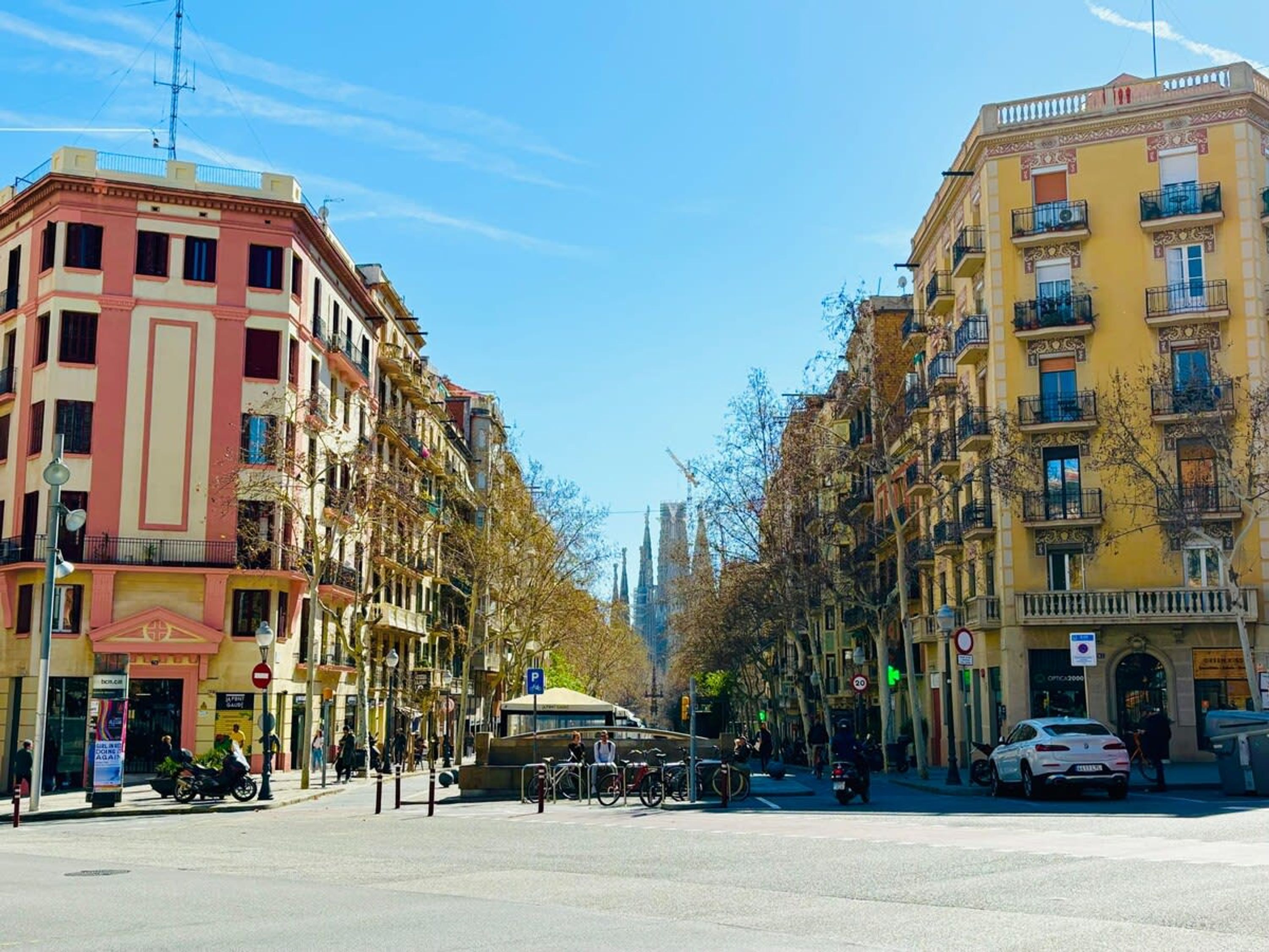 A street view with multi-story buildings, a clear sky, and a tram in the distance.