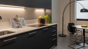 A modern kitchen with dark cabinetry, a built-in sink, and a dining area with a table and chairs. - Sant Pau Patio 2BR Near Avinguda Gaud With Patio (Barcelona)