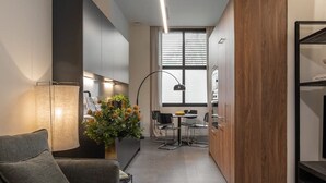 A modern living room with a sofa, a coffee table, and a lamp. There is a kitchen area with cabinets and a window. - Sant Pau Patio 2BR Near Avinguda Gaud With Patio (Barcelona)