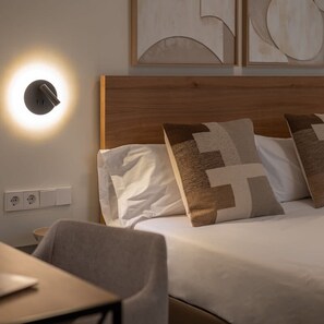 A neatly made bed with patterned pillows, a bedside table, and a wall-mounted light fixture.