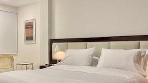 A neatly made bed in a hotel room with a headboard, a bedside lamp, a small table, and a chair. - w Fantastic 2BR Apartment w AC in Cartagena (Cartagena)