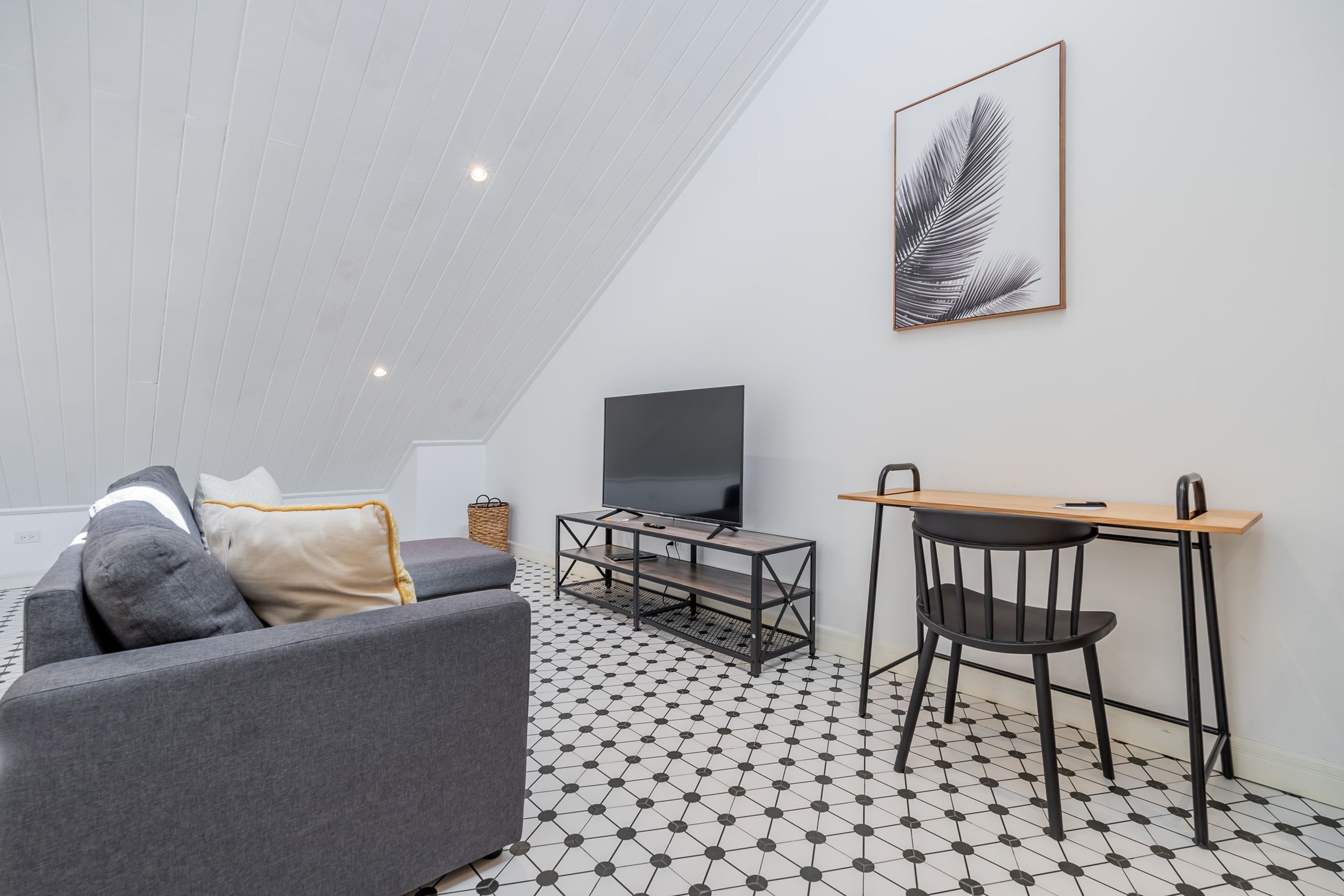 A modern living room with a sofa, a TV, a desk, and a chair.