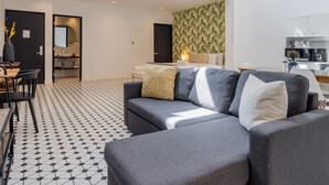 Un soggiorno moderno con un divano grigio, un'area pranzo con tavolo e sedie, una cucina e una parete decorata.