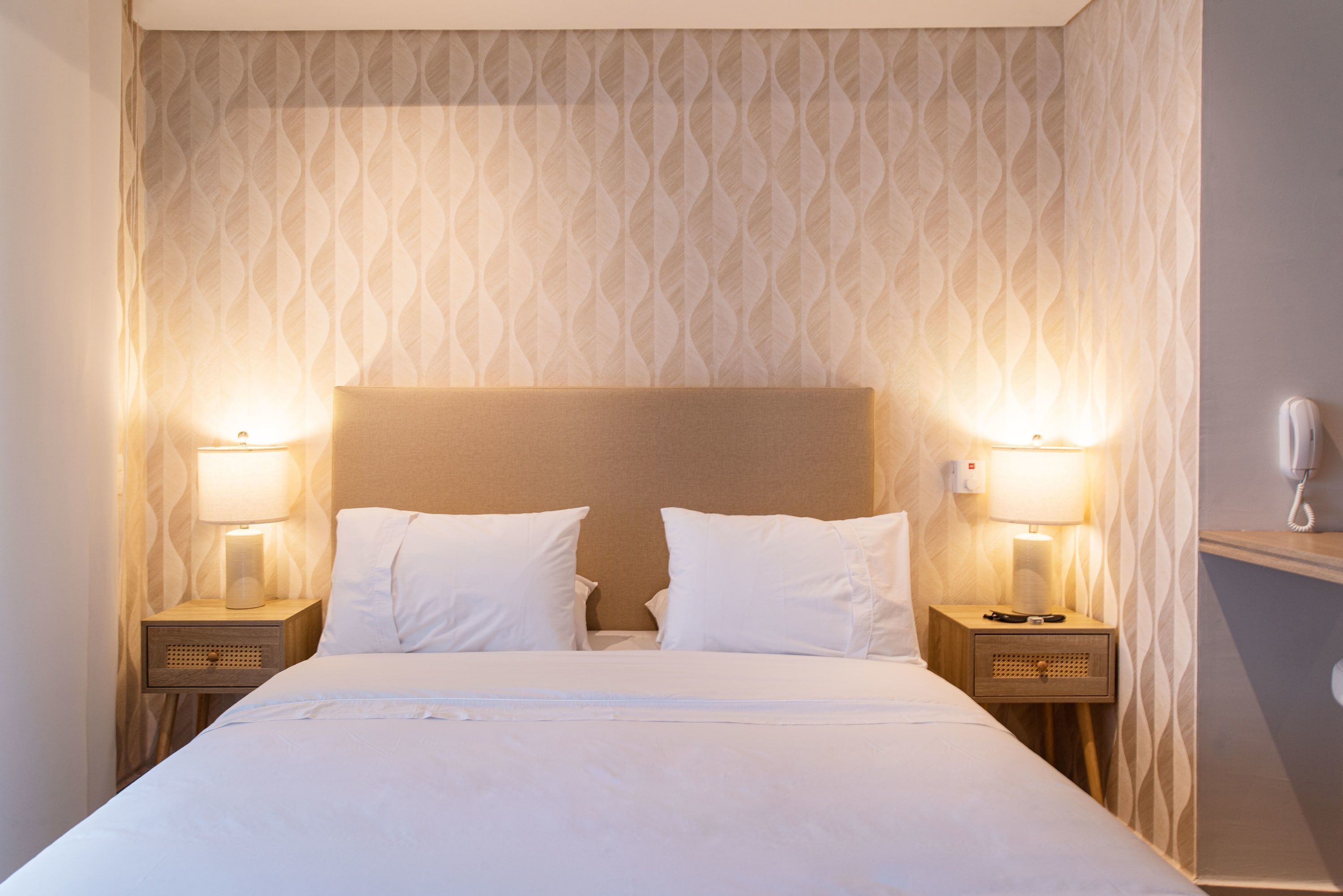 A neatly made bed with white linens, two bedside tables with lamps, and a patterned wallpaper.