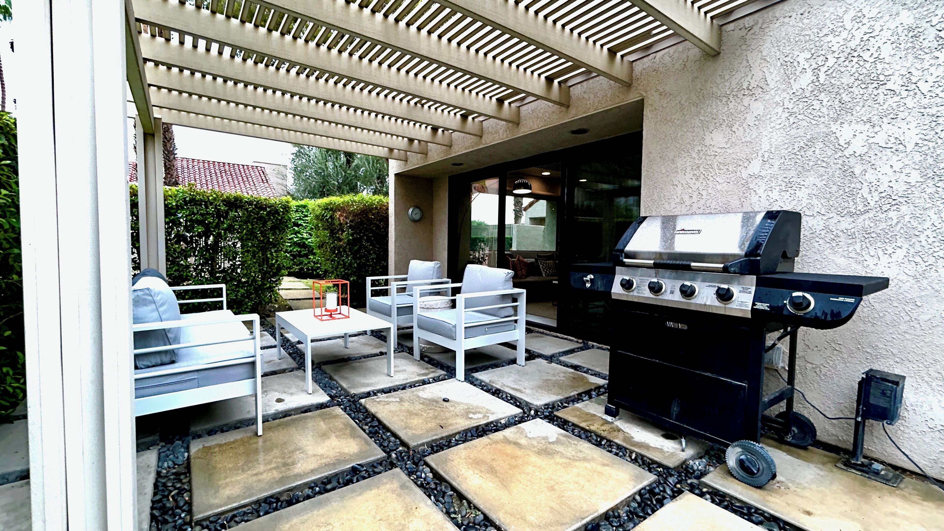 Un patio al aire libre con una parrilla, sillas blancas y una mesa.