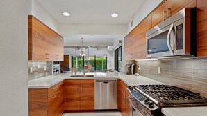 A modern kitchen with wooden cabinets, stainless steel appliances, and a view to the outdoors.