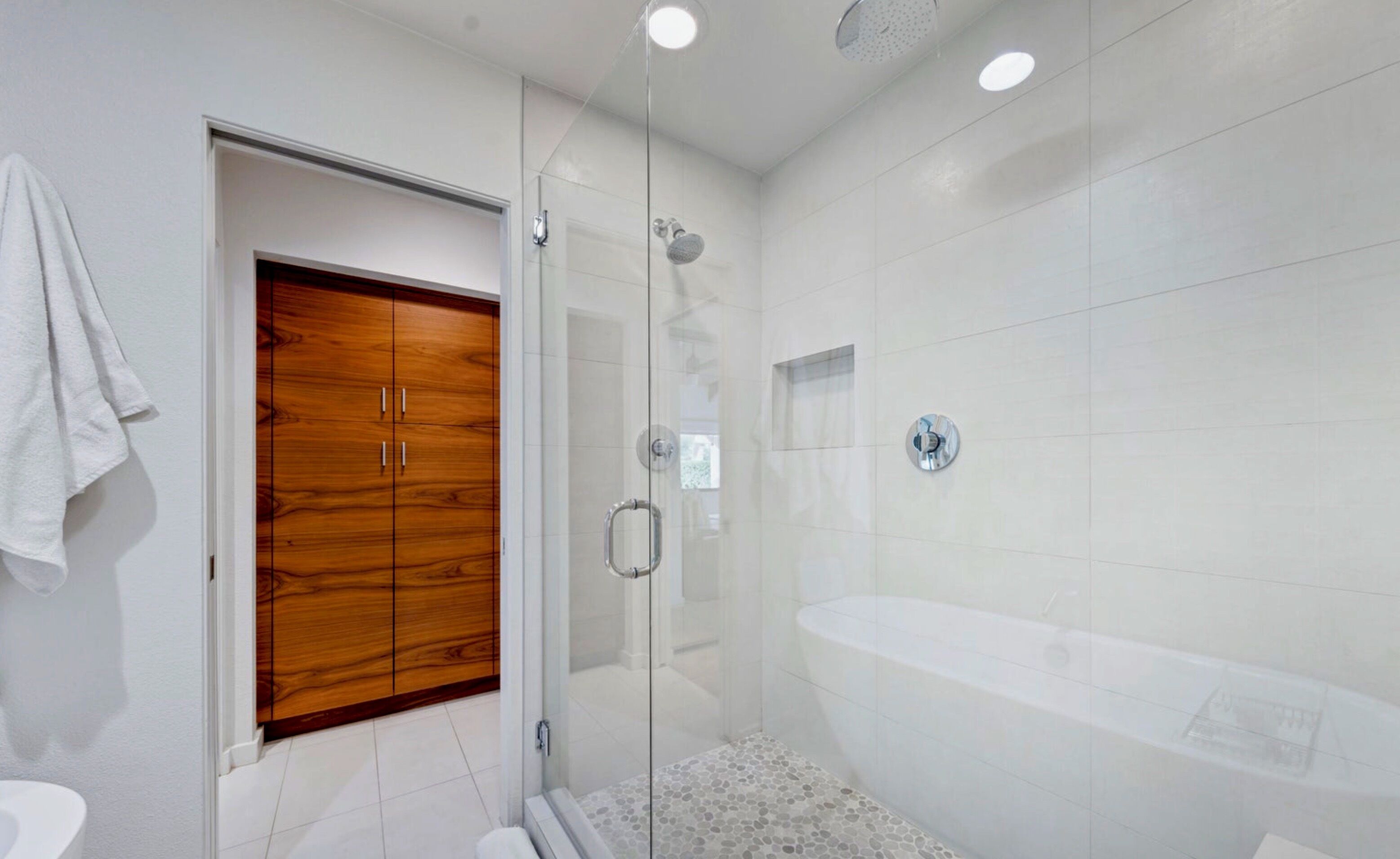 A modern bathroom with a glass-enclosed shower, a wooden wardrobe, and a freestanding bathtub.