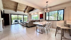 A spacious living area with a dining table, chairs, a sofa, and a TV mounted on the wall.