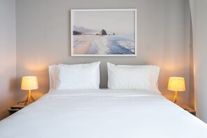A neatly made bed with white linens, two bedside lamps, and a framed coastal landscape painting on the wall. - w Wonderful Loft With Terrace in La Boquilla (Cartagena)