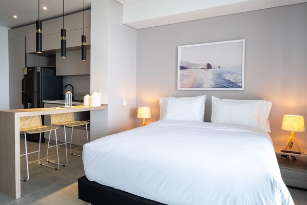 A modern hotel room with a large bed, a desk with two bar stools, a refrigerator, and a painting of a beach scene on the wall. - w Wonderful Loft With Terrace in La Boquilla (Cartagena)