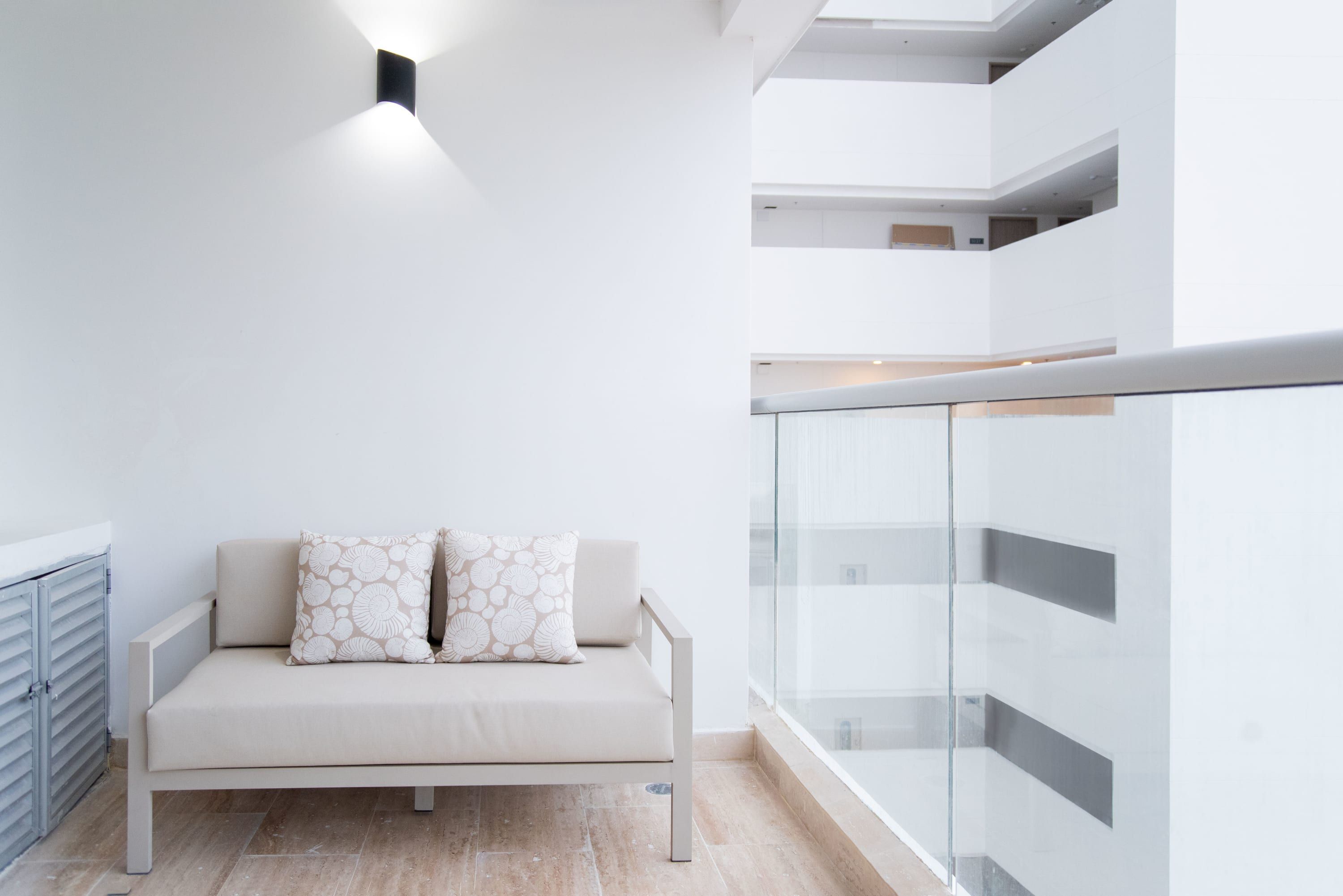 A modern, minimalist living area with a sofa and patterned cushions, a glass railing, and a clean, white interior.
