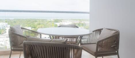 A balcony with wicker chairs and a table, overlooking a cityscape.