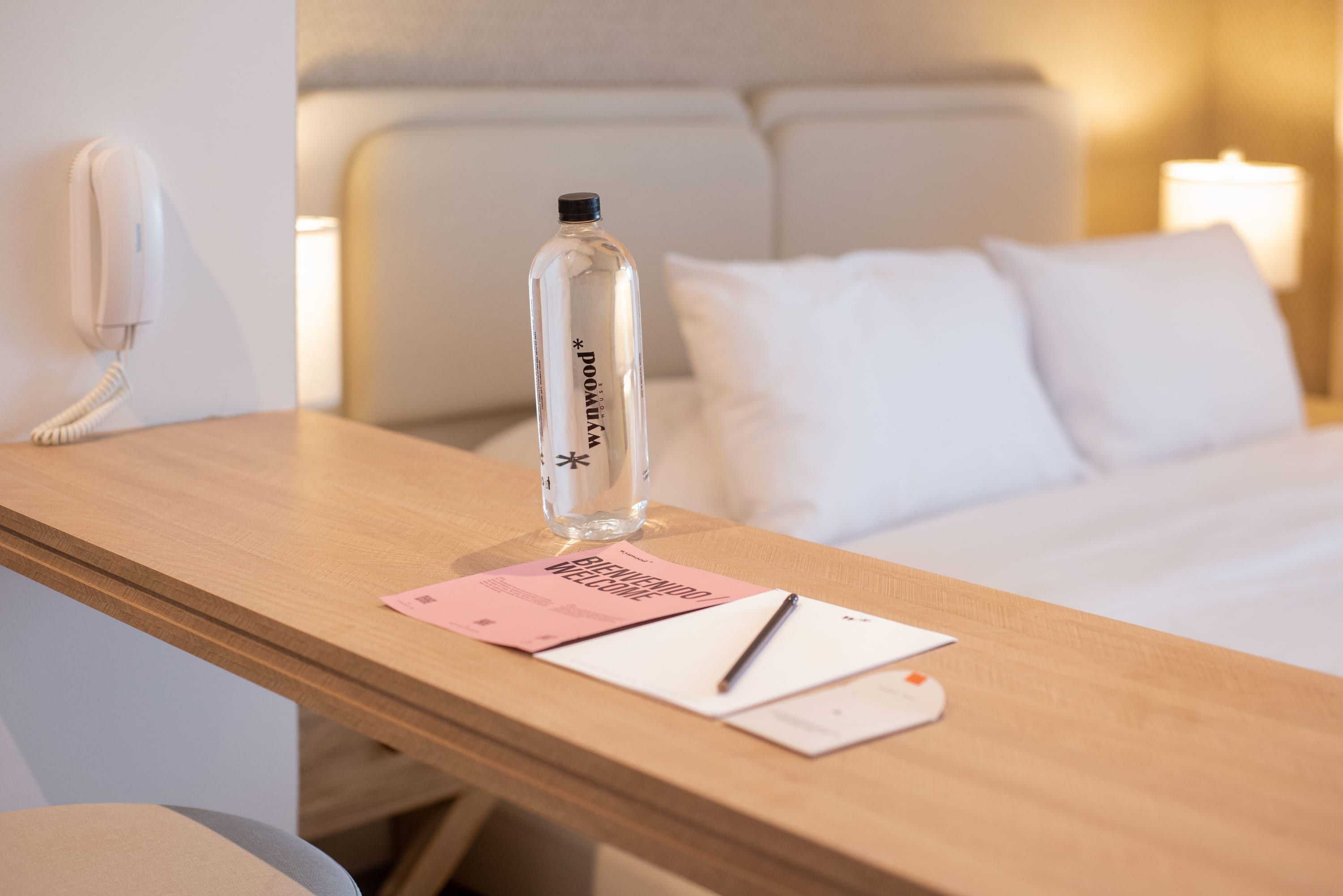 A hotel room with a wooden desk, a bottle of water, a welcome card, and a pen.