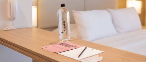 A hotel room with a wooden desk, a bottle of water, a welcome card, and a pen.