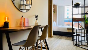 Ein modernes Hotelzimmer mit einem Holztisch, zwei Stühlen, einem runden Spiegel und einem Bett mit Blick auf die Stadt.