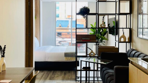 Ein modernes Hotelzimmer mit einem Bett, einer schwarzen Couch, einem Esstisch und einer Küchenzeile.