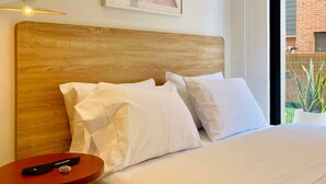 A hotel room with a wooden headboard, white bedding, a small round table with a remote control, and a framed abstract artwork on the wall. - w Phenomenal Loft With Modern Deco in Bogota (Bogotá)