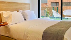 A hotel room with a large bed, a wooden headboard, a framed abstract artwork, and a view of a brick building and outdoor seating area through a glass door. - w Phenomenal Loft With Modern Deco in Bogota (Bogotá)