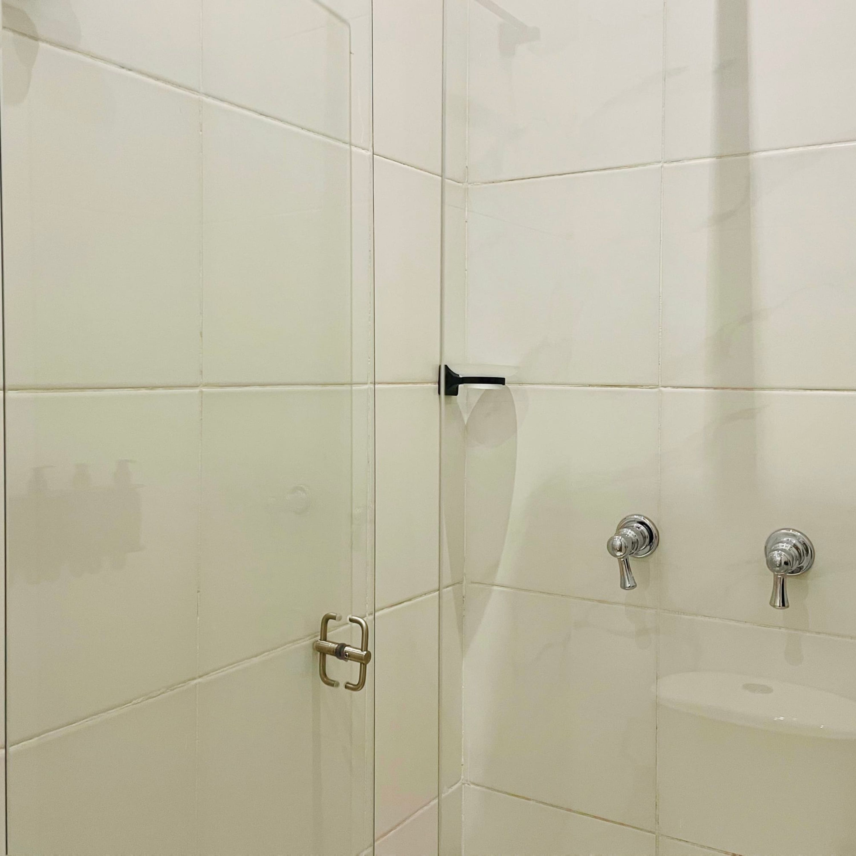 Un baño con azulejos blancos, una ducha con cabezal de ducha manual y un lavabo con grifo.