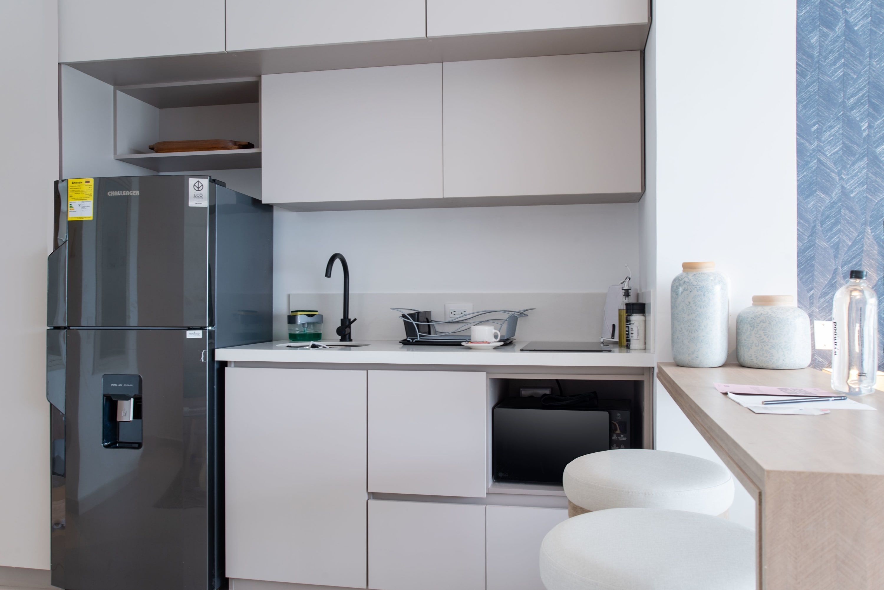 Een moderne keuken met een roestvrijstalen koelkast, witte keukenkastjes, een spoelbak en een aanrecht met potten en een waterfles.
