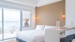 Et moderne soveværelse med en stor seng, et skrivebord og udsigt til en balkon gennem en skydedør.