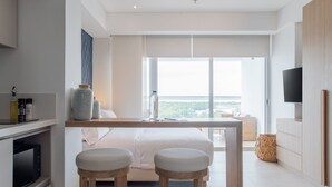 Et moderne hotelværelse med en stor seng, to barstole, et fjernsyn og en balkon med udsigt over byen.