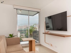 En moderne stue med en stor skydedør til en balkon, et stort fladskærms-tv på væggen, en beige sofa og et lille træbord.