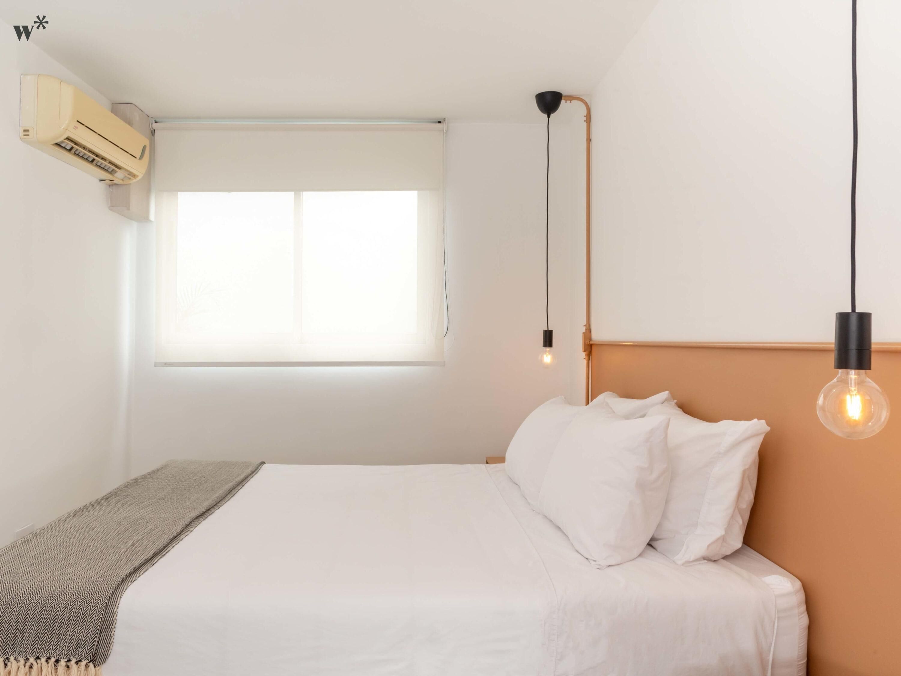 Une chambre à coucher avec un lit, une fenêtre, un climatiseur et un luminaire suspendu.