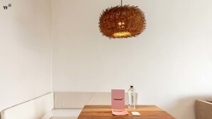 Ein Holztisch mit einem rosafarbenen Schild, einer klaren Flasche und einer gewebten Pendelleuchte in einem minimalistischen Raum.