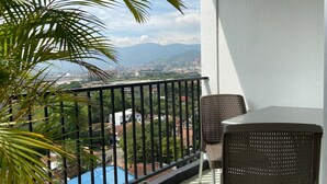 A balcony with a view of a cityscape, a pool, and a palm tree. - w Magnificent 1BR With Terrace at Poblado (Medellín)