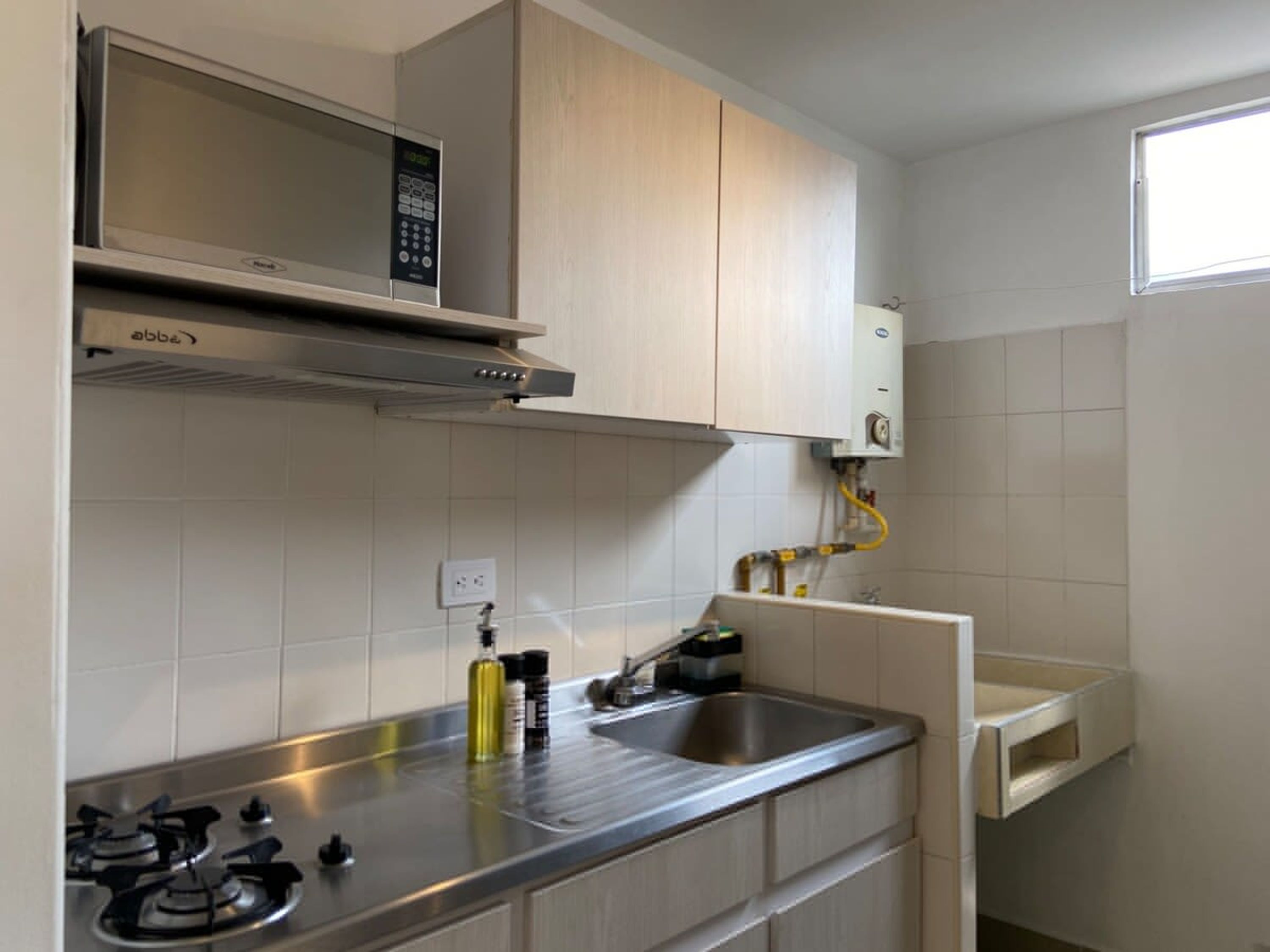 Een moderne keuken met een inbouwmagnetron, gasfornuis en een klein spoelbakje.
