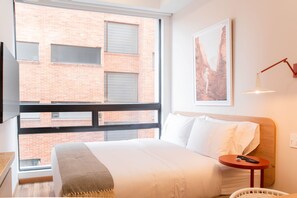 A hotel room with a large window, a bed, a bedside table with a lamp, and a wall-mounted picture. - w Awesome Loft With Modern Deco in Bogota (Bogotá)